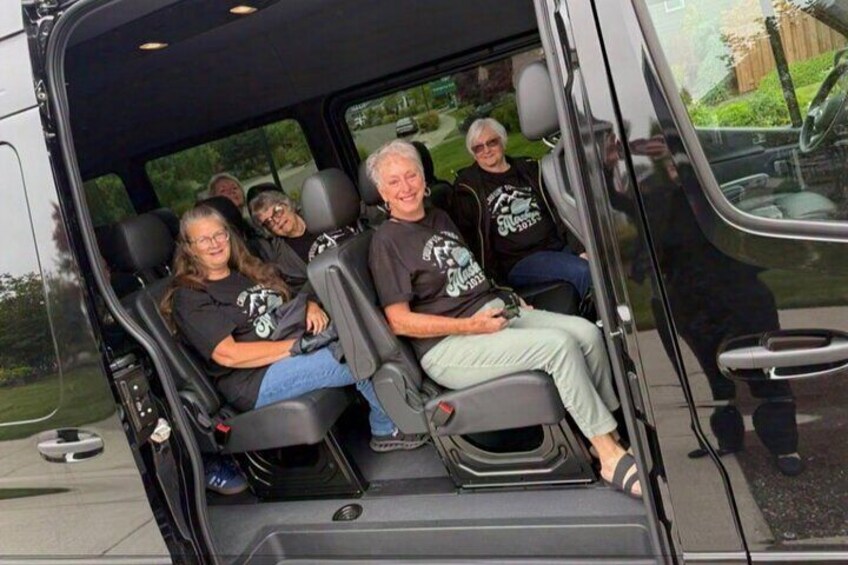 A group of people seated inside a vehicle with a black interior and a visible steering wheel. 5