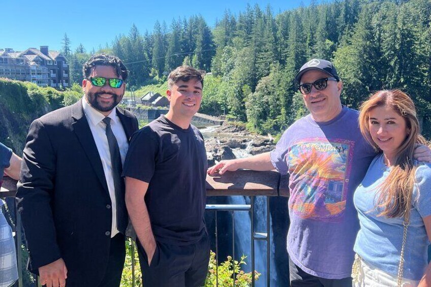 Four people standing outdoors near a railing with a forested background. 2