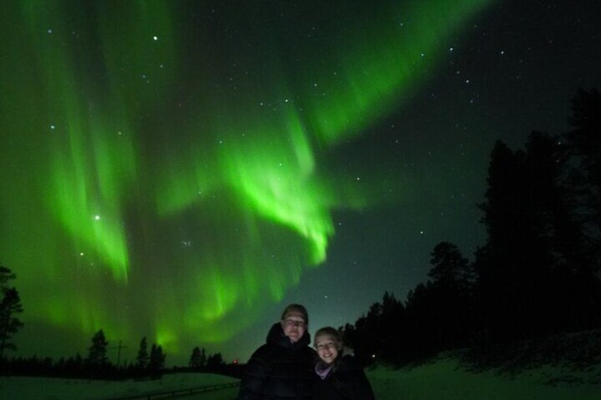 Two people standing in a snowy landscape with the Northern Lights in the background. 4