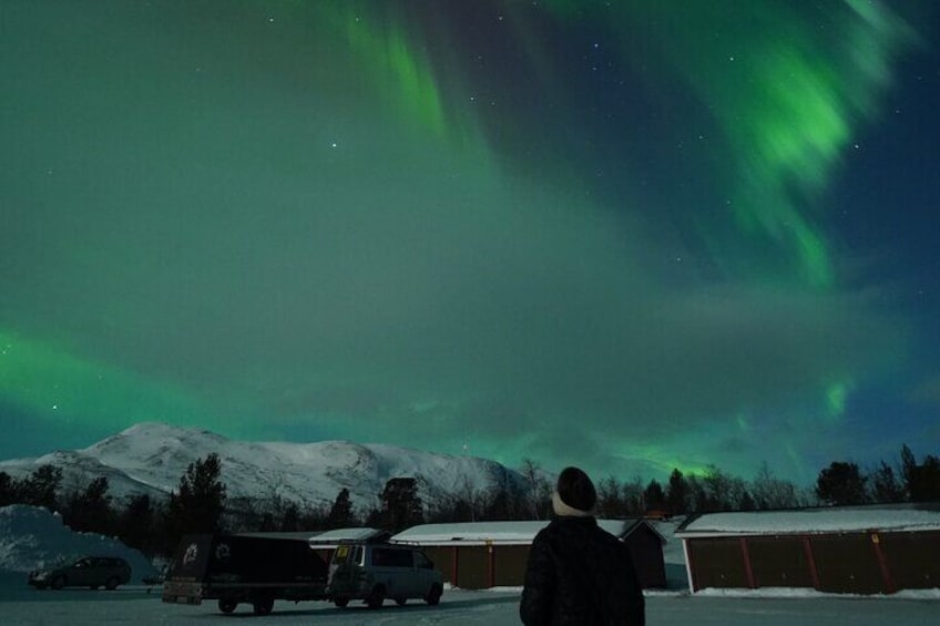 A person observing the Northern Lights over a snowy landscape with buildings in the background. 5