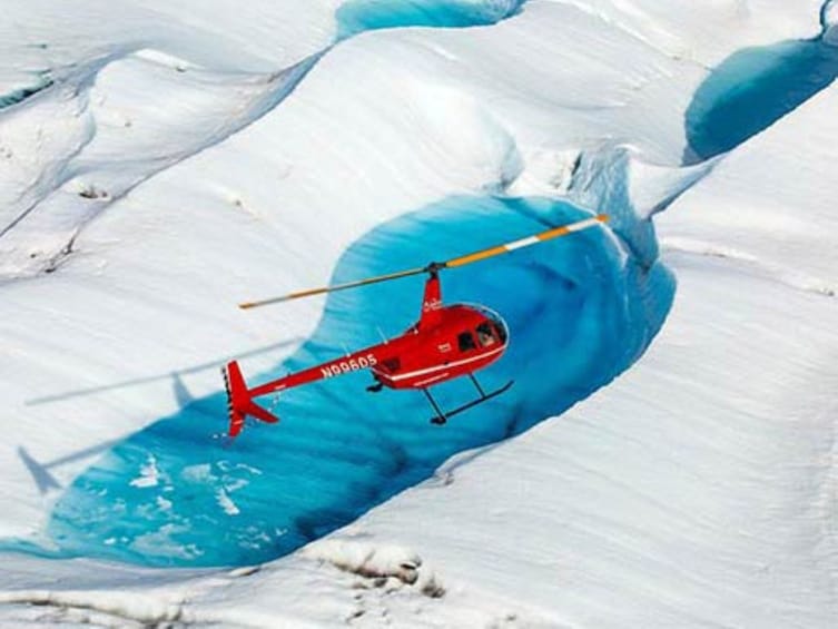 A red helicopter flying over a glacier. 1