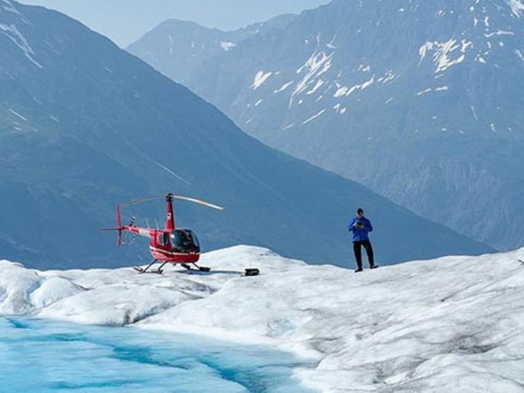 A red helicopter on a snowy mountain with a person standing nearby. 4