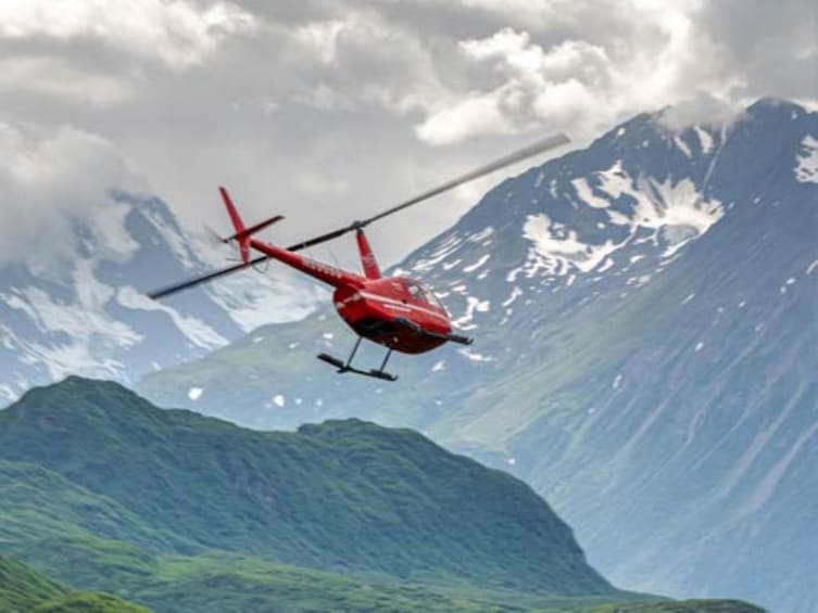 A red helicopter flying over a mountainous landscape with snow-capped peaks. 5