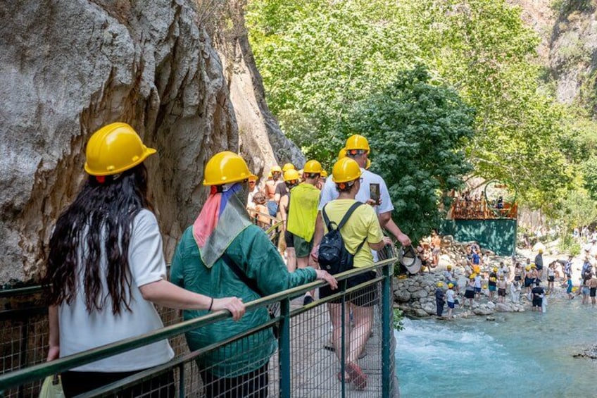 People wearing yellow helmets and green uniforms near a rocky cliff and a river. 2