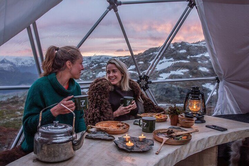 Deux personnes sont assises à une table à l’intérieur d’une tente, avec vue sur des montagnes enneigées. 4