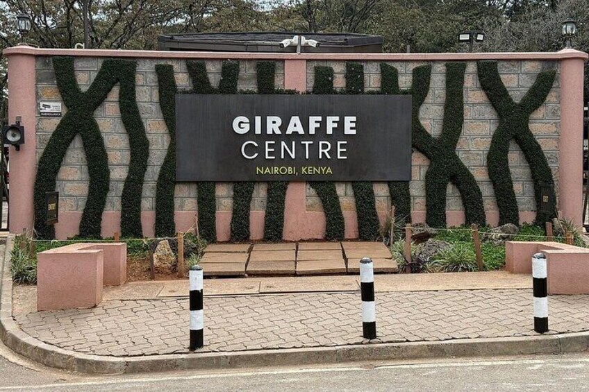 A sign for the Giraffe Centre in Nairobi, Kenya, with a brick wall and green foliage. 1