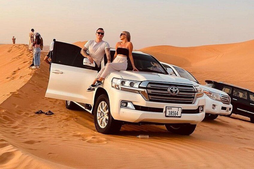 A white SUV parked on a sand dune with a desert landscape in the background. 1