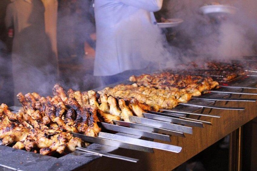 A barbecue grill with skewers of meat, steam rising, and a person in the background. 2