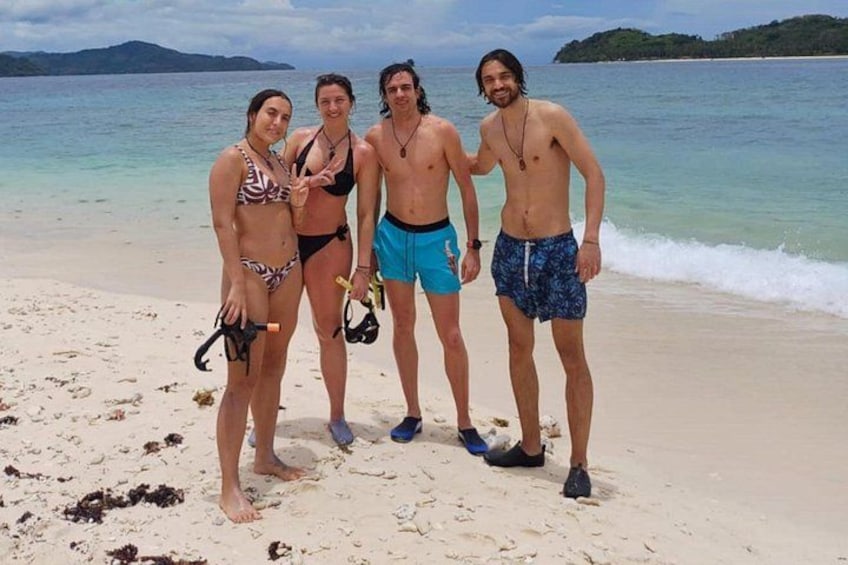 A beach with four people standing, one holding a camera. 2