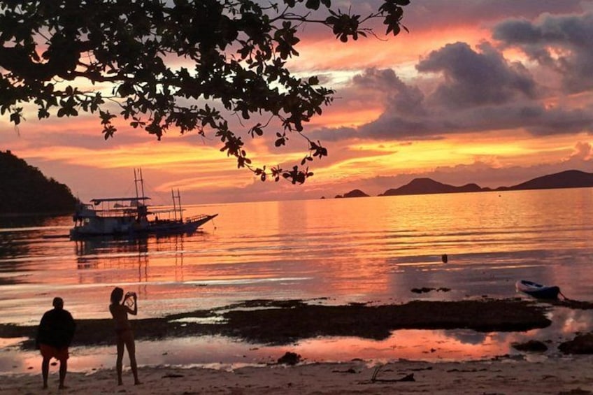 A sunset over a calm body of water with boats and a person standing on the shore. 4