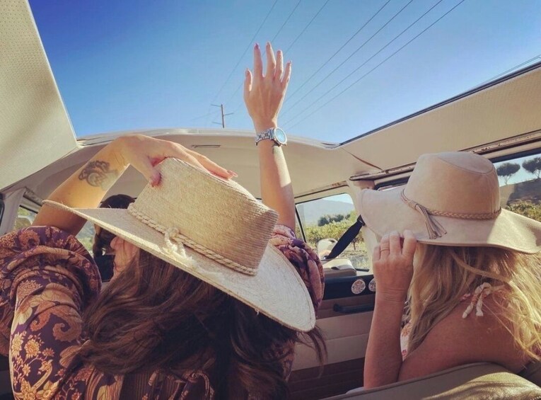 Two people in a convertible car, one holding a hat. 4