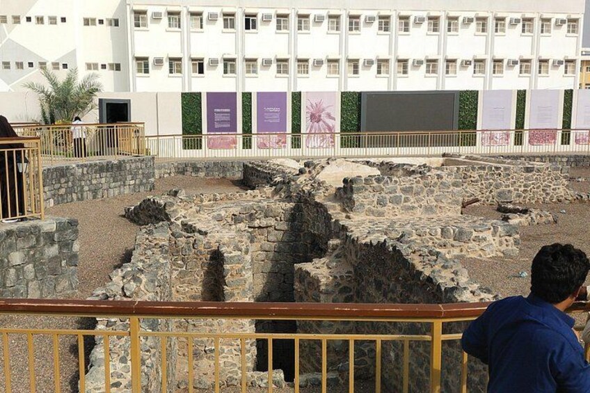 An archaeological site with stone ruins and a modern building in the background. 2
