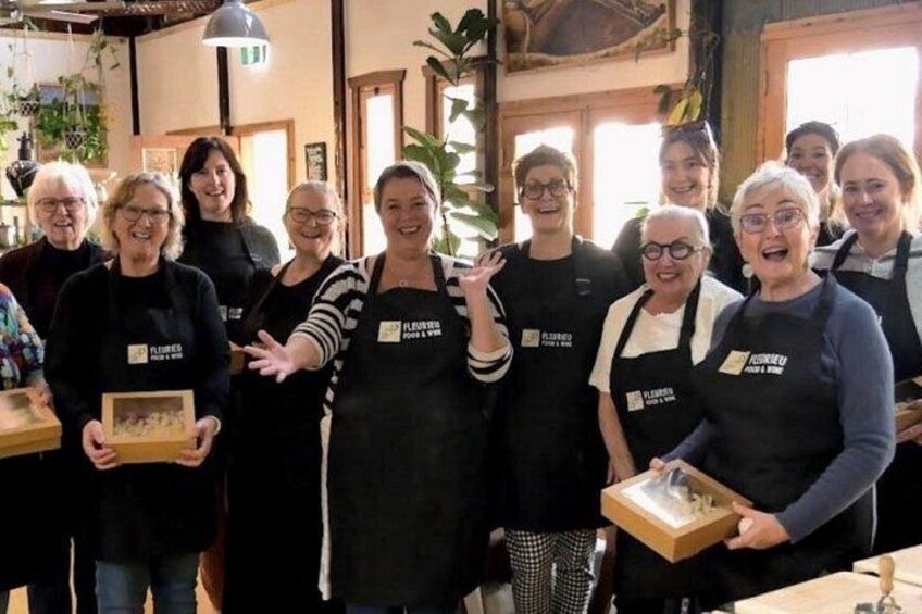 A group of people in aprons with 'FLOUR & LOVE' text, holding awards in a room with wooden beams and plants. 2