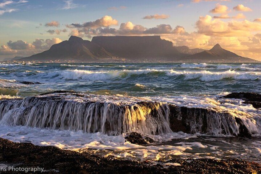 A coastal scene with waves crashing onto rocks, a waterfall, and a mountain range in the background. 3
