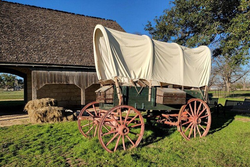 A covered wagon with red wheels parked in front of a rustic building. 5