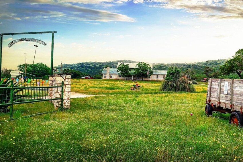 A rural landscape with a green metal gate, a wooden trailer, and a house in the background. 2