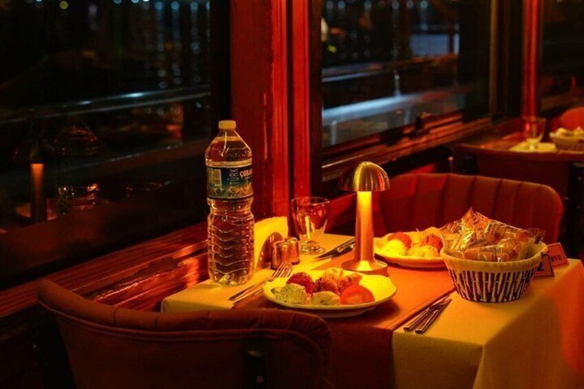 A table with a bottle of water, a basket of bread, and a plate of food in a dimly lit restaurant. 2