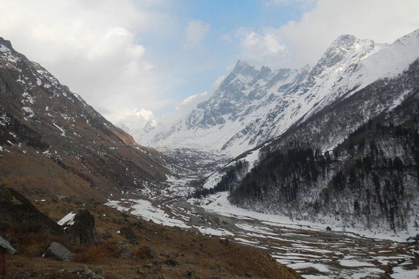 A mountainous landscape with snow-covered peaks, a valley with a river, and a forested area. 1