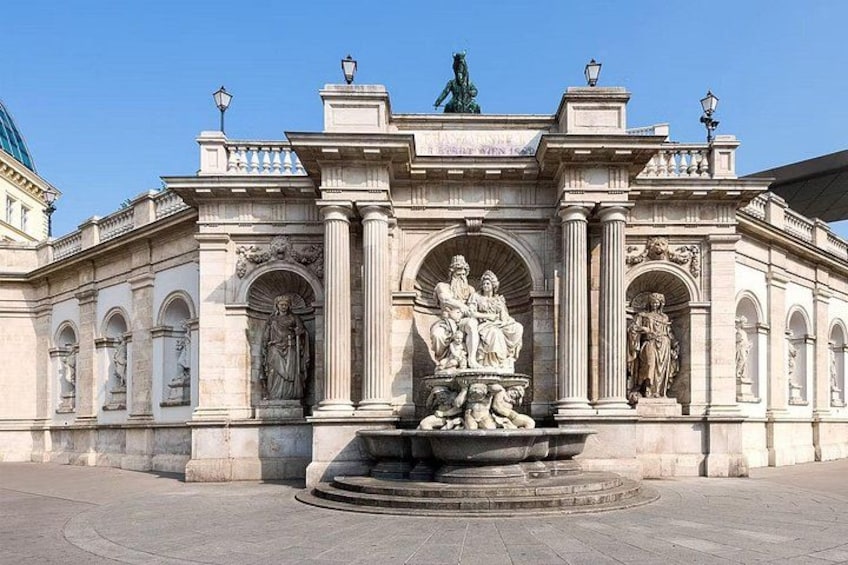 Ein klassizistisches Gebäude mit einer zentralen Fontäne, Statuen und einem aufwendigen Eingang. 1