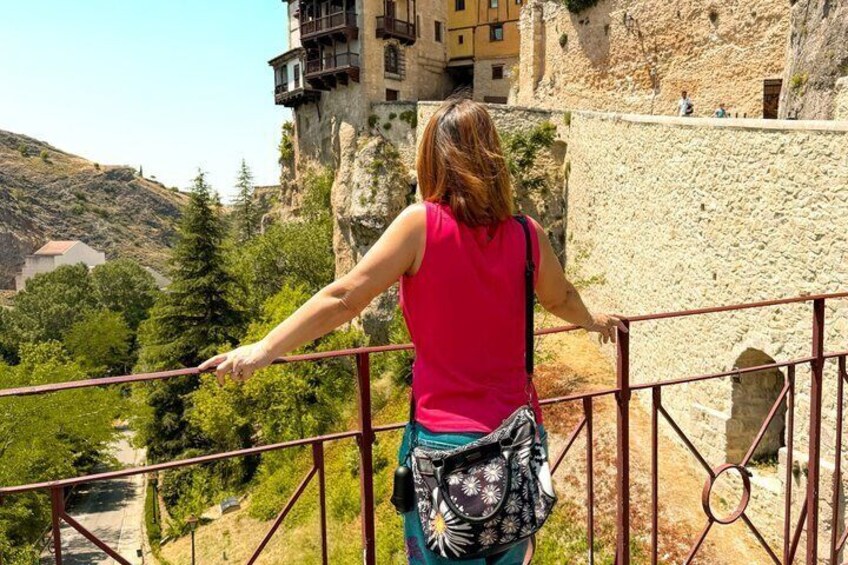 Una persona está de pie en un balcón con vista a un paisaje montañoso y un edificio en el acantilado. 2