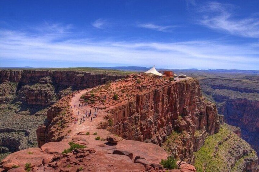 A canyon with a white tent on a cliff edge and a trail leading down. 5