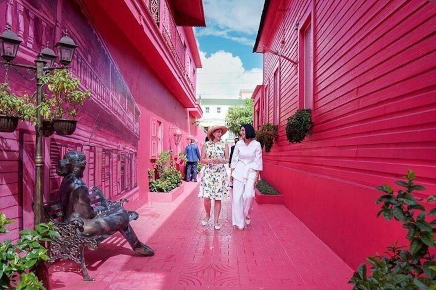 A narrow alley with red buildings, a statue of a seated figure, and a person walking. 5