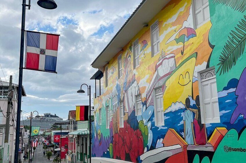 A colorful mural on a building, a flag, and a ship in the background. 2