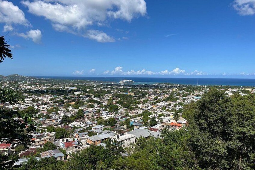 A coastal cityscape with dense housing, a clear blue sky, and a distant view of the ocean. 3