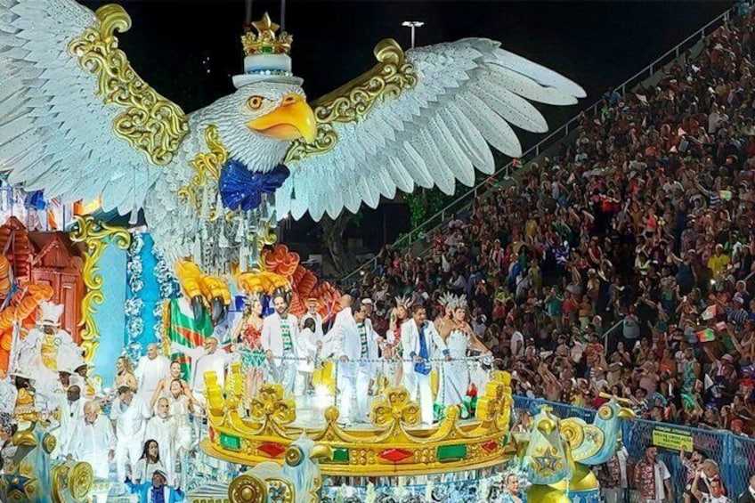 A large crowd at a nighttime outdoor event with a prominent eagle float. 5