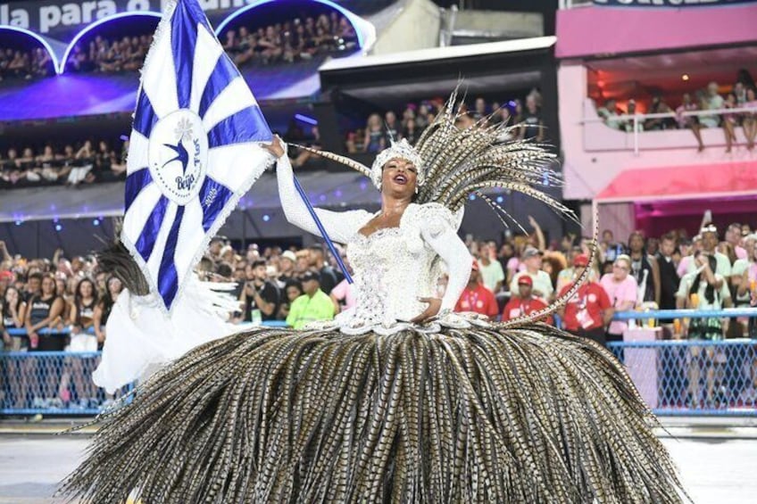 A performer in a large, ornate costume with a fan and flag, on a parade float. 1