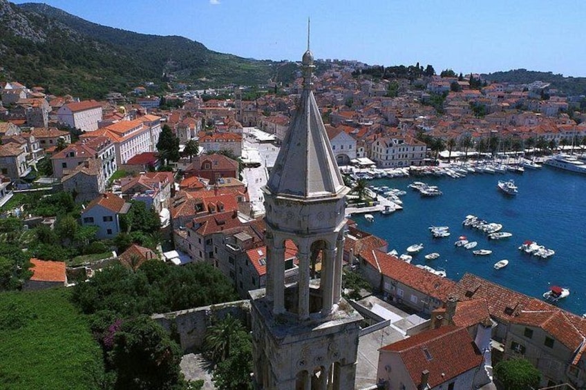 Un pueblo costero con una torre de iglesia destacada, un puerto deportivo con barcos y un paisaje montañoso de fondo. 3