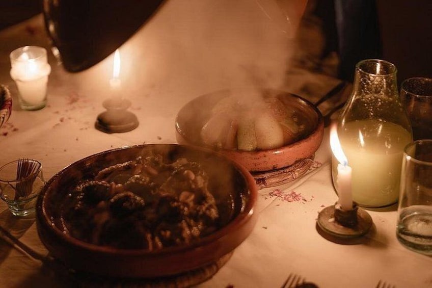 A dimly lit dining table with a bowl of food, a candle, and a bottle. 2