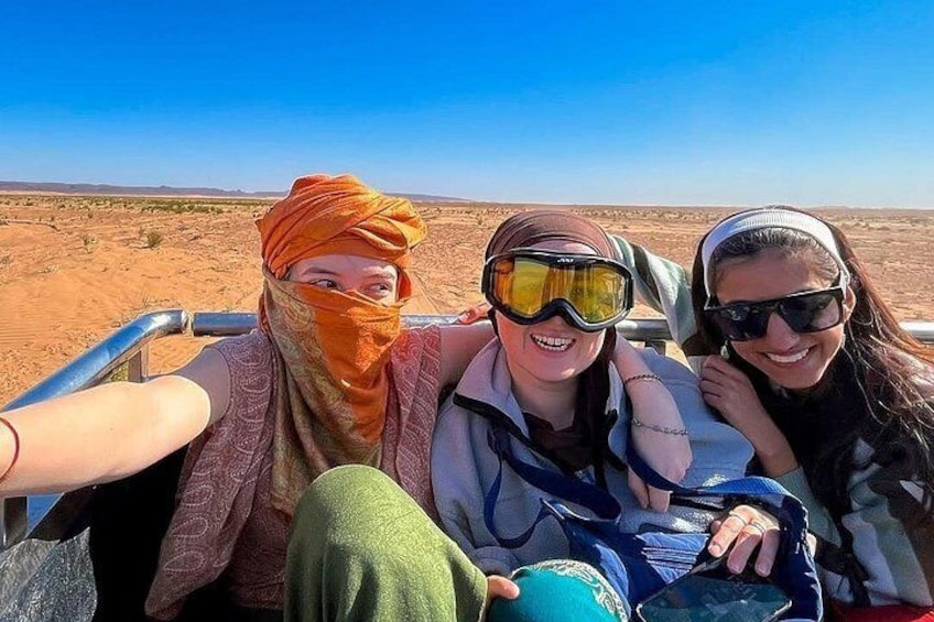 Three people in a desert setting, wearing casual clothing and head coverings. 1