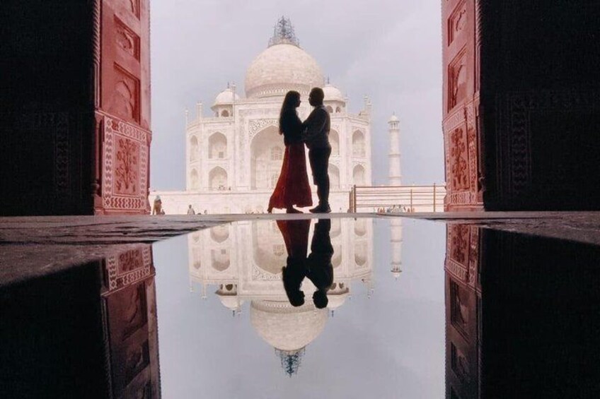 A couple standing in front of the Taj Mahal with its reflection in the water. 4