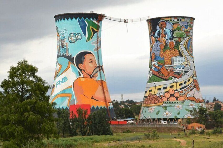 Dos estructuras cilíndricas grandes con murales coloridos, rodeadas de follaje y un cielo nublado. 3