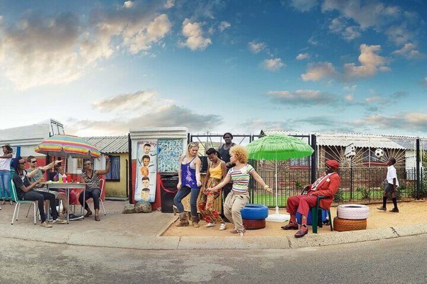 Un mercado callejero con gente sentada y de pie bajo sombrillas, un puesto de comida y una valla con una portería de fútbol. 4