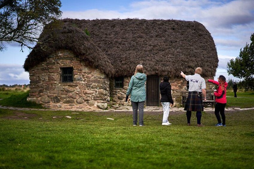 A thatched-roof stone house with people standing in front of it. 2
