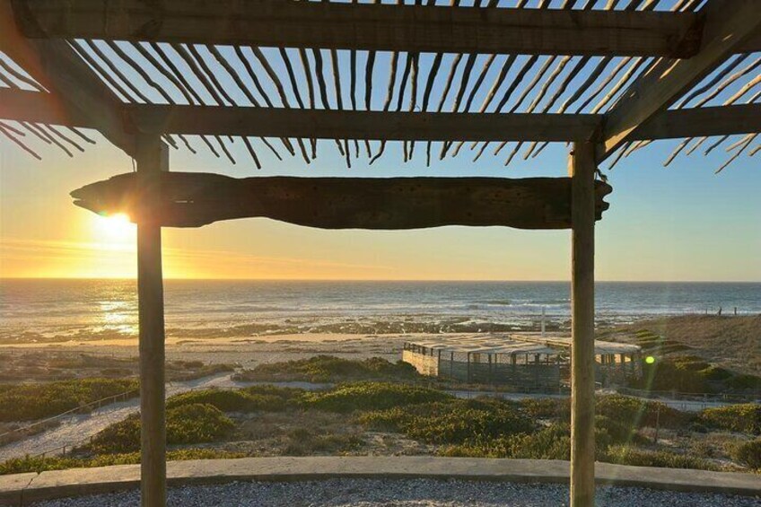 A beach view with a wooden pergola, ocean, and a small building in the distance. 3