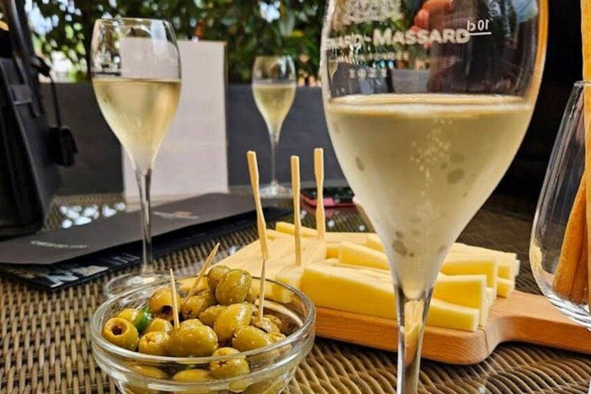 A table with a bowl of olives, a cheese board, and glasses of white wine. 5