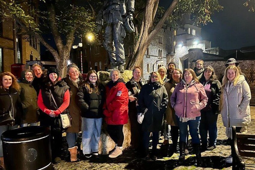 A group of people standing outdoors at night near a statue and a building. 5