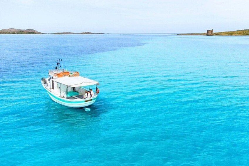 A boat on clear turquoise water with a distant island and a small structure on the shore. 1