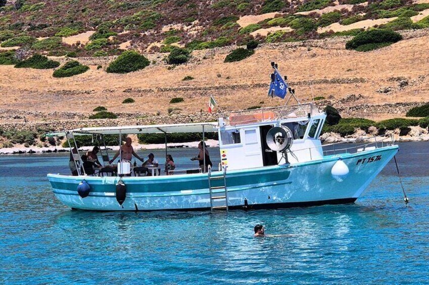A small boat with people on board, anchored near a rocky shoreline. 4