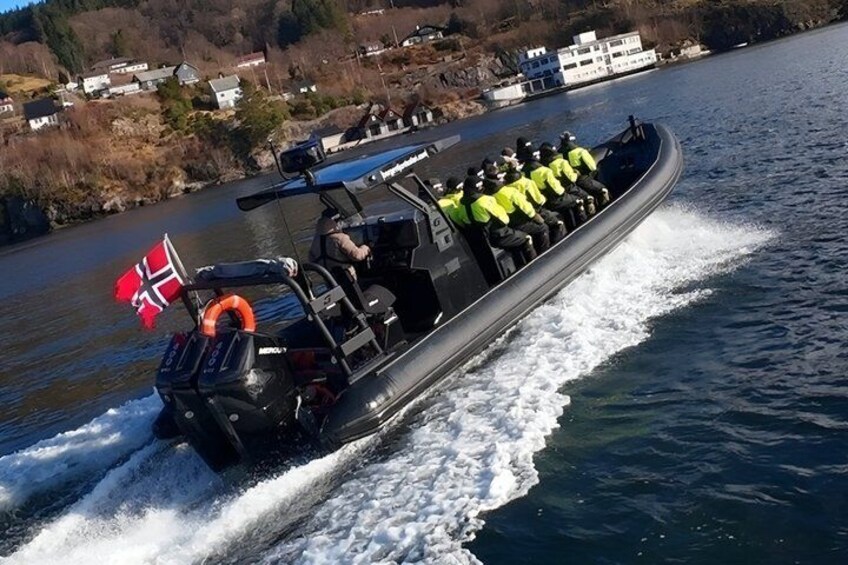 Un bateau à moteur arborant le drapeau norvégien, une personne portant un blouson jaune, et une rivière avec des maisons en arrière-plan. 3