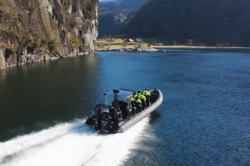 Un bateau rempli de personnes vêtues de couleurs vives, naviguant sur un lac paisible, entouré de falaises. 1