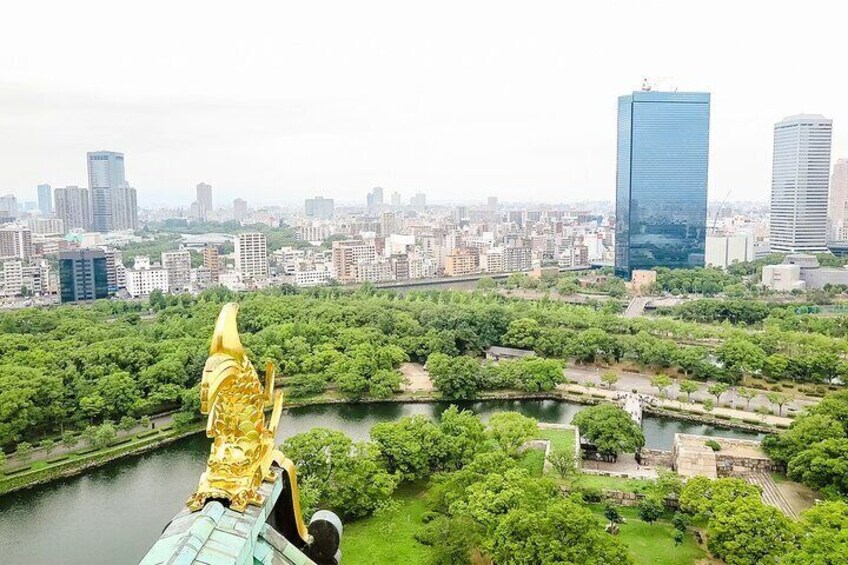 A golden statue overlooking a cityscape with a river and greenery. 3