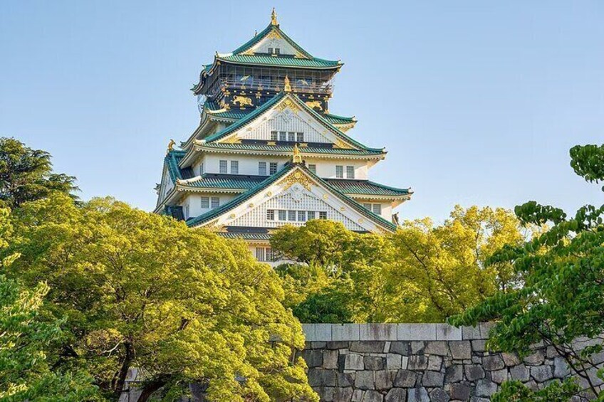 A traditional Japanese castle with multiple tiers, surrounded by lush green trees. 1