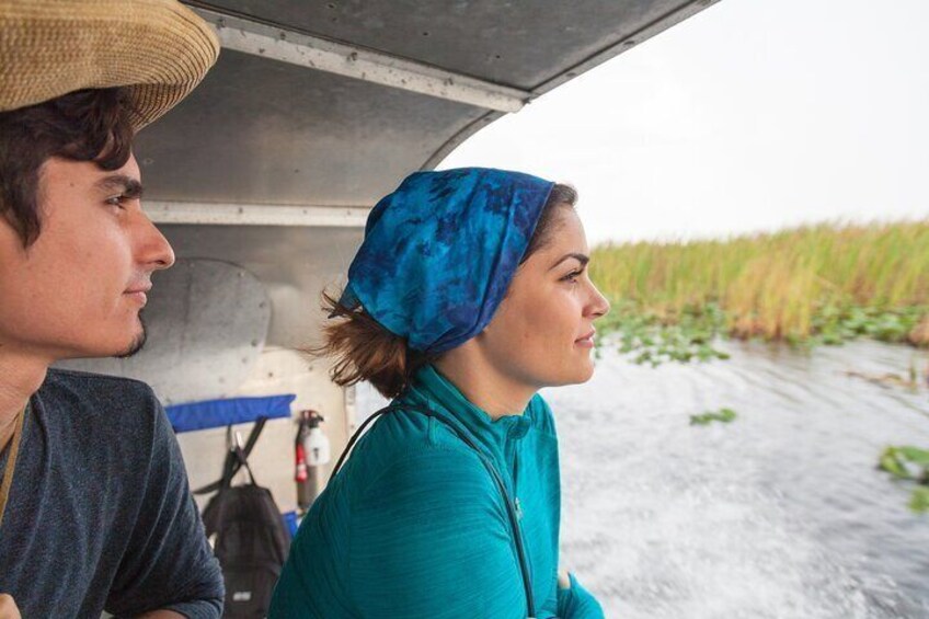 Twee personen in een boot, één draagt een strohoed, en een wateroppervlak met vegetatie op de achtergrond. 4