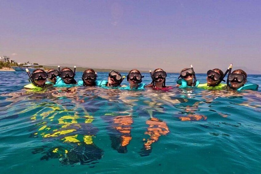 A group of people snorkeling in clear blue water with a beach and ocean in the background. 3