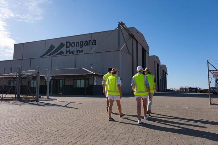 Un grande edificio industriale con il cartello 'Dongara Marine' e un'area recintata con persone che indossano giubbotti di sicurezza. 4
