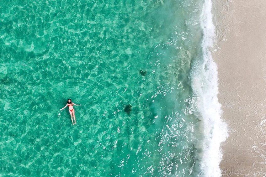 A person floating in clear turquoise water near a sandy beach with gentle waves. 4